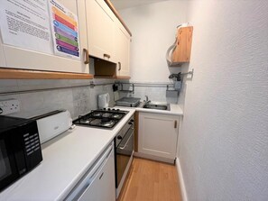 A compact kitchen with a gas stove, microwave, and a sink. - 2 Bed in Aberdyfi (oc-dy017) (Aberdovey)