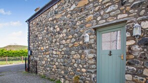 Ein Steinhaus mit einer grünen Tür, einem kleinen Blumentopf und einem Laternen an der Wand.
