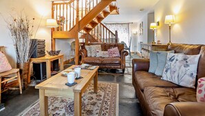 Ein gemütliches Wohnzimmer mit einer Holztreppe, einem braunen Ledersofa, einem Holztisch und einem gemusterten Teppich.