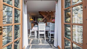Ein Eingangsbereich mit Steinboden und einer Holztreppe, die zu einem Essbereich mit weißen Stühlen und einem Tisch führt.