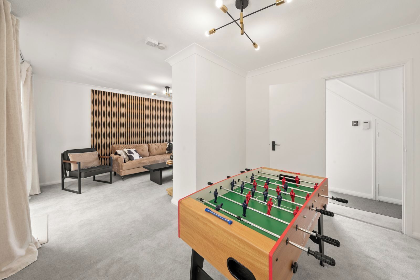A room with a foosball table, a sofa, and a patterned wall.