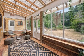 A room with a patterned floor, wicker furniture, and a view of a garden through large windows. - Stylish home I sleeps 8 I free parking (Virginia Water)