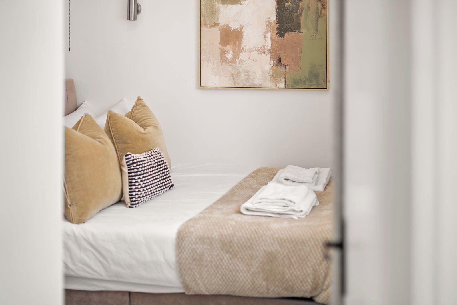 A neatly made bed with a white comforter, beige pillows, and a striped pillow. A folded towel is placed on a beige blanket on the bed.