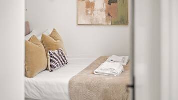 A neatly made bed with a white comforter, beige pillows, and a striped pillow. A folded towel is placed on a beige blanket on the bed.