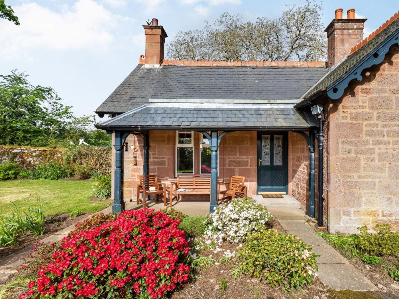 A stone house with a covered porch, a bench, and a flower bed.