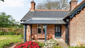 A stone house with a covered porch, a bench, and a flower bed. - 2 Bed in Kirriemuir (oc-86235) (Logie)