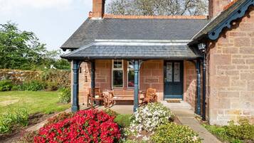 A stone house with a covered porch, a bench, and a flower bed.