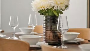 Ein Esstisch, gedeckt mit Tellern, Schüsseln und Weingläsern, mit einer Blumenvase in der Mitte.