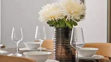 A dining table set with plates, bowls, and wine glasses, with a vase of flowers in the center.