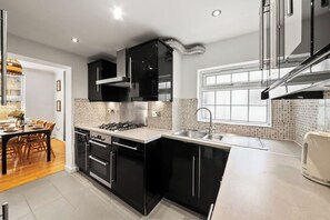 Eine moderne Küche mit schwarzen Schränken, einem Gasherd, einem Kombi-Backofen und einer Spüle aus Edelstahl.