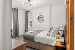 Ein modernes Schlafzimmer mit Bett, Nachttischlampe und Spiegel an der Wand.