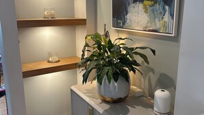 Un bagno moderno con un mobile bagno in legno, una pianta in vaso, un quadro astratto incorniciato e uno scaffale con oggetti decorativi.