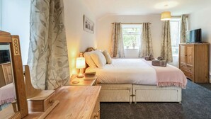 Ein Hotelzimmer mit Bett, Nachttisch, Lampe, Fernseher, Kleiderschrank und einem Fenster mit Vorhängen.