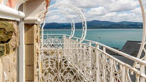 A balcony with ornate white metal railings overlooking a body of water and distant mountains. - 2 Bed in Aberdyfi (oc-dy039) (Aberdovey)