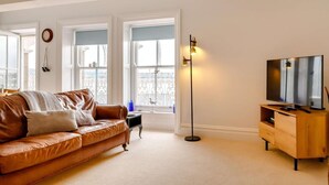 A living room with a brown leather sofa, a television on a wooden stand, and a floor lamp. - 2 Bed in Aberdyfi (oc-dy039) (Aberdovey)