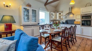 Zona pranzo con tavolo in legno apparecchiato per quattro persone, circondato da sedie, in una stanza con pavimento in legno e mobili da cucina bianchi.