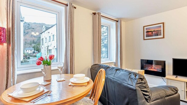 Ein gemütliches Zimmer mit Esstisch für zwei Personen, einer Couch, einem Fernseher und einem Fenster mit Blick auf Gebäude.