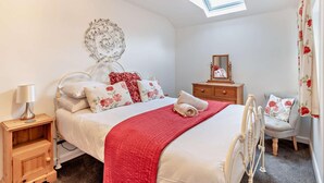 Ein Schlafzimmer mit Bett, Nachttisch, Kommode, Spiegel, Stuhl und Dachfenster.