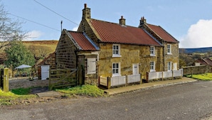 A stone house with a red-tiled roof, a wooden fence, and a gravel driveway. - 1 Bed in Whitby (oc-86298) (Castleton)