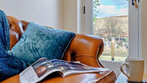 A leather sofa with a magazine, a white mug, and a window with a view of hills. - 1 Bed in Whitby (oc-86298) (Castleton)