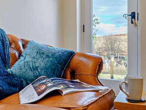 A leather sofa with a magazine, a white mug, and a window with a view of hills. - 1 Bed in Whitby (oc-86298) (Castleton)