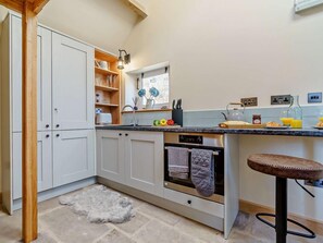 A kitchen with white cabinets, a built-in oven, a bar stool, and a window with flowers. - 1 Bed in Whitby (oc-86298) (Castleton)