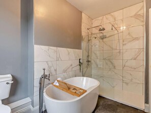 Een badkamer met een vrijstaand bad, een douche met glazen wanden en marmeren tegels.