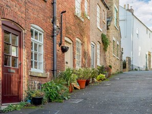 A narrow street with red brick buildings, a red door, and potted plants along the sidewalk. - 2 Bed in Matlock (oc-86418) (Wirksworth)