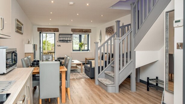Eine moderne Küche mit integrierten Geräten, ein Essbereich mit einem Holztisch und Stühlen sowie eine Treppe mit grauer Geländer.