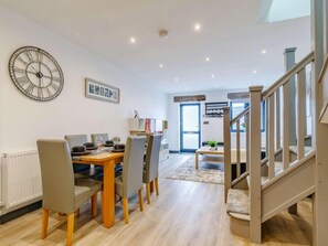 A modern living room with a dining area, wooden flooring, a staircase, and a large wall clock. - 2 Bed in Matlock (oc-86418) (Wirksworth)