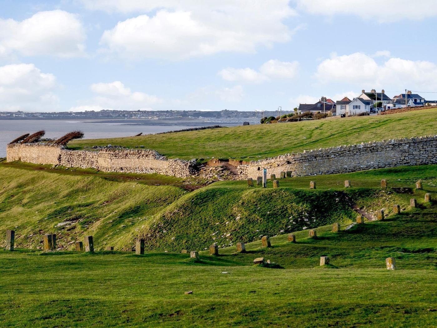 A coastal landscape with stone walls, grassy fields, and a stone cross.