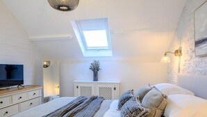 A bedroom with a skylight, a television, a dresser, a bedside table with a lamp, and a bed with patterned pillows. - 3 Bed in Bridgend (oc-86494) (Southerndown)