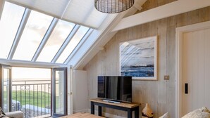 A modern living room with a TV, sofa, coffee table, and artwork on a wooden wall. - 3 Bed in Bridgend (oc-86494) (Southerndown)