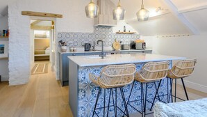 A compact kitchen with a central island, bar stools, and hanging pendant lights. - 3 Bed in Bridgend (oc-86494) (Southerndown)