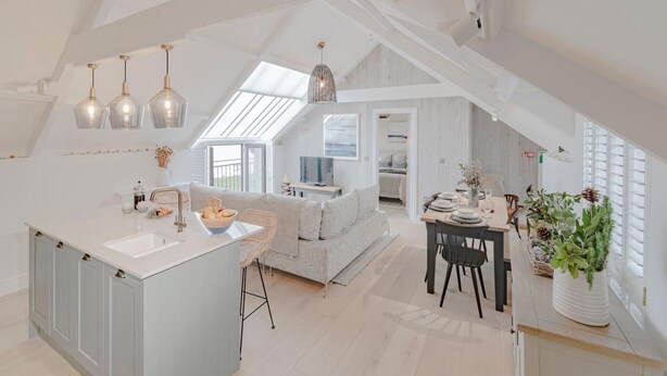A spacious loft with a kitchen, dining area, and living space, featuring skylights and modern furnishings. - 3 Bed in Bridgend (oc-86494) (Southerndown)