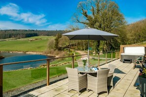 Eine Terrasse mit Korbmöbeln, einem Whirlpool und Blick auf einen See und Golfplatz.