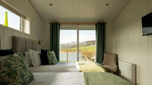 A room with two beds, a chair, a view of a lake, and a window with curtains. - 2 Bed in Castle Douglas (oc-86449) (Auchencairn)