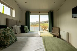 A room with two beds, a chair, a view of a lake, and a window with curtains.