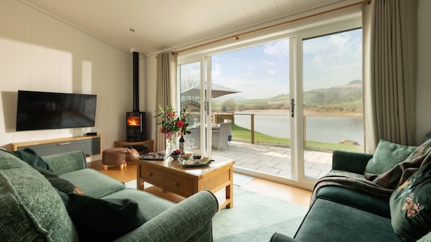 A living room with a TV, fireplace, and a view of a lake. - 2 Bed in Castle Douglas (oc-86449) (Auchencairn)