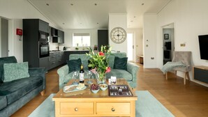 A modern living room with a sofa, coffee table, and a dining area with a clock on the wall. - 2 Bed in Castle Douglas (oc-86449) (Auchencairn)