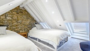A bedroom with two beds, a stone wall, and a sloped ceiling. - 2 Bed in Bridgend (oc-86495) (Southerndown)