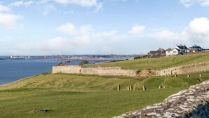 A coastal landscape with a stone wall, grassy hill, and houses in the background. - 2 Bed in Bridgend (oc-86495) (Southerndown)
