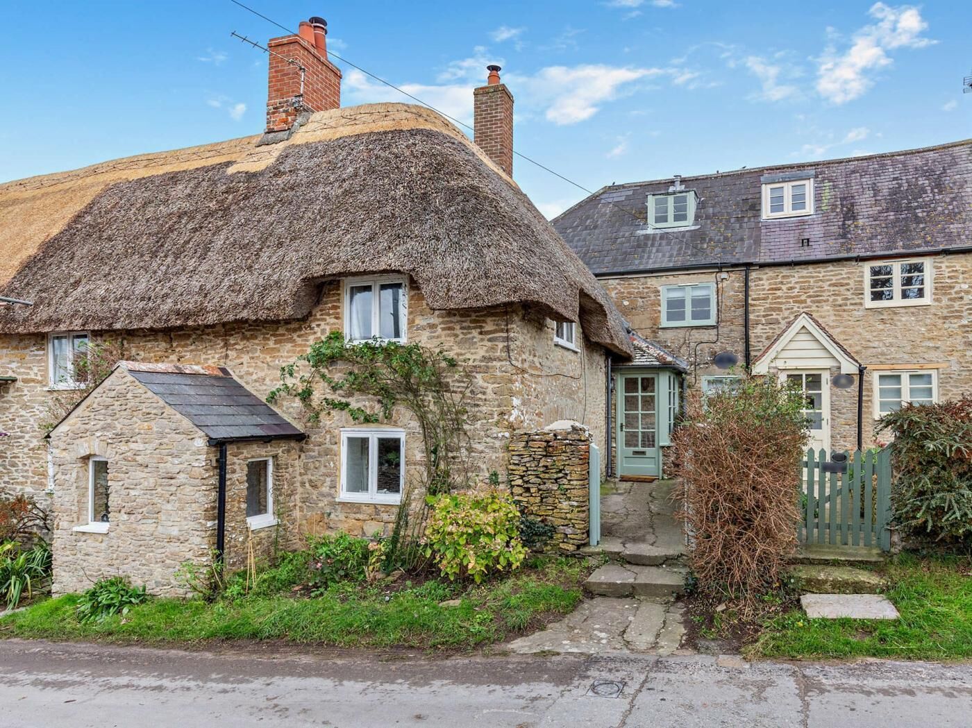 A stone house with a thatched roof and a smaller stone extension.