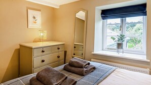 Um quarto com uma cama, penteadeira, espelho, janela com vista e um quadro na parede.