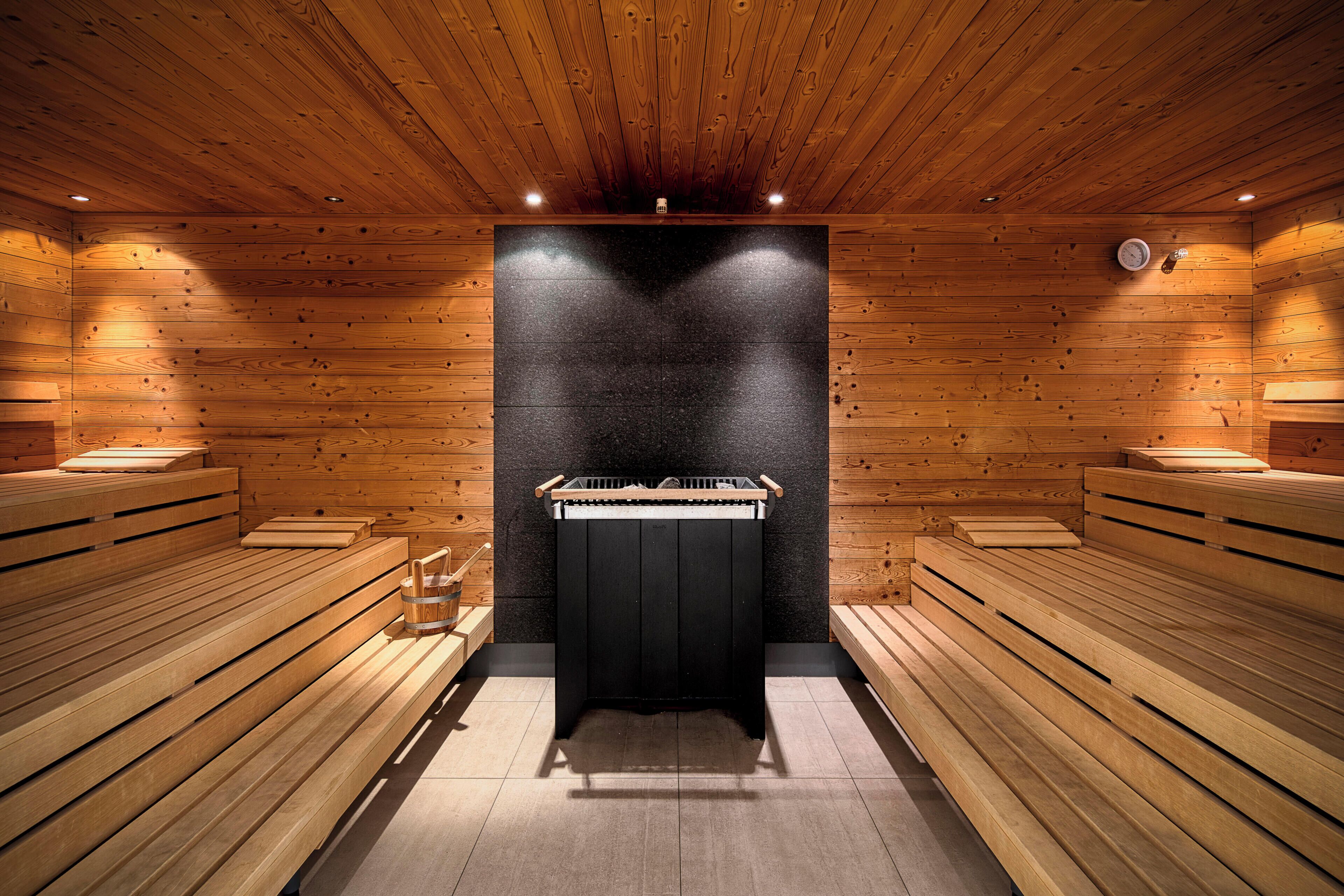 A sauna room with wooden benches, a central table, and a black wall.