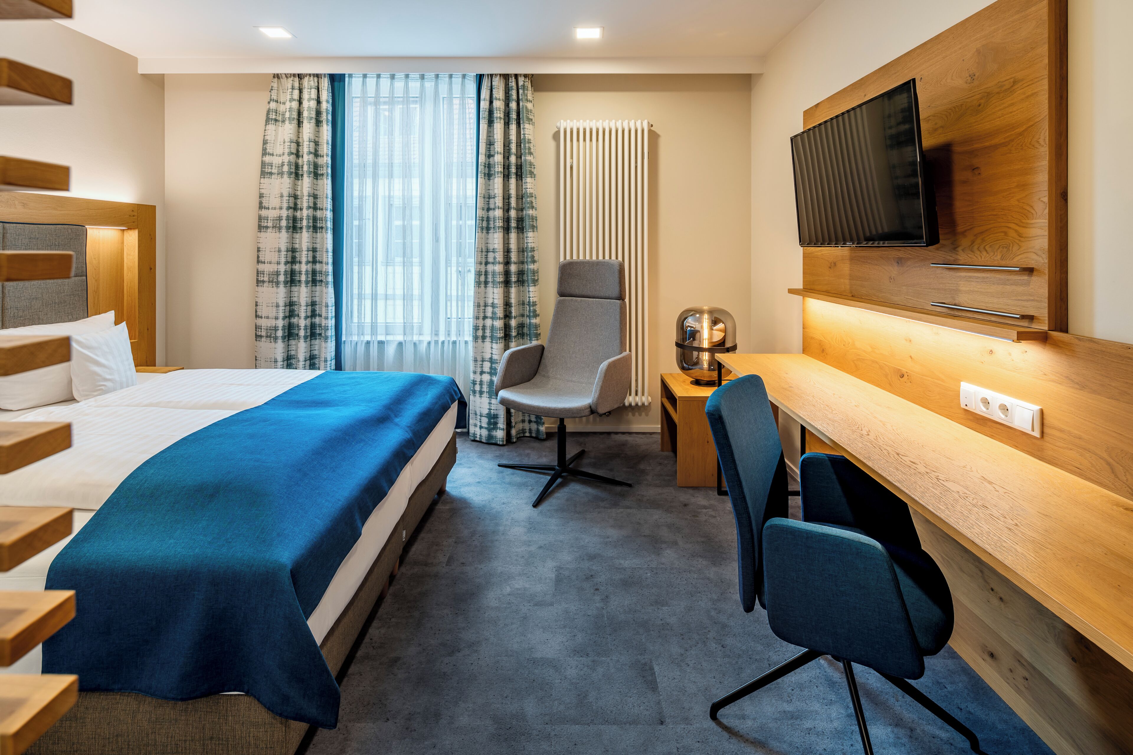A hotel room with a bed, a desk, a chair, a television, and a radiator.