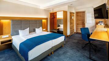Ein Hotelzimmer mit Bett, Schreibtisch, Sessel, Fernseher und Kleiderschrank.