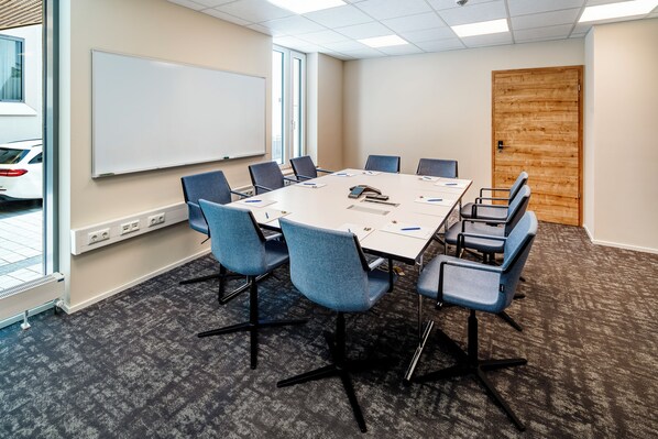 A conference room with a white table, blue chairs, a whiteboard, and a wooden door.