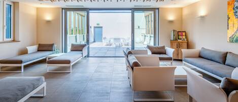 A modern hotel lobby with seating areas, a coffee station, and a view of the outdoor patio.