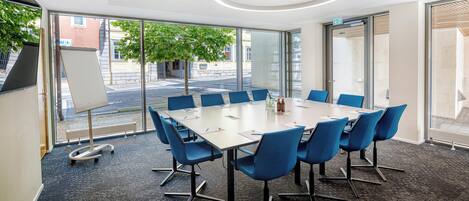 Ein Konferenzraum mit einem großen Tisch, blauen Stühlen und einer Wandtafel.